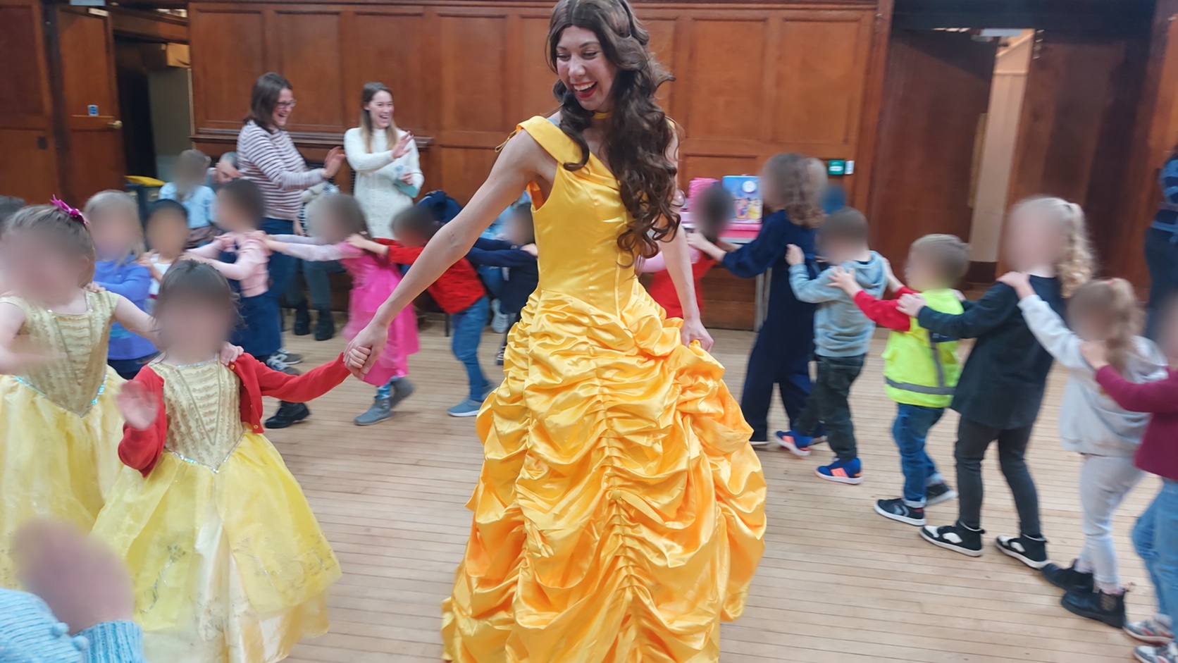 A princess performer leading children in a party dance, with children’s faces blurred