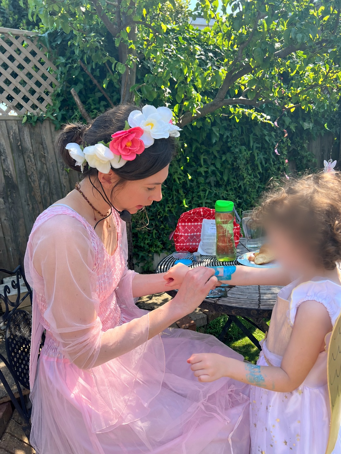 A fairy performer painting a child’s arm outdoors, with the child’s face blurred